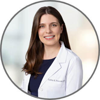Dr Primeau wearing a white lab coat, smiling against a softly blurred light background.